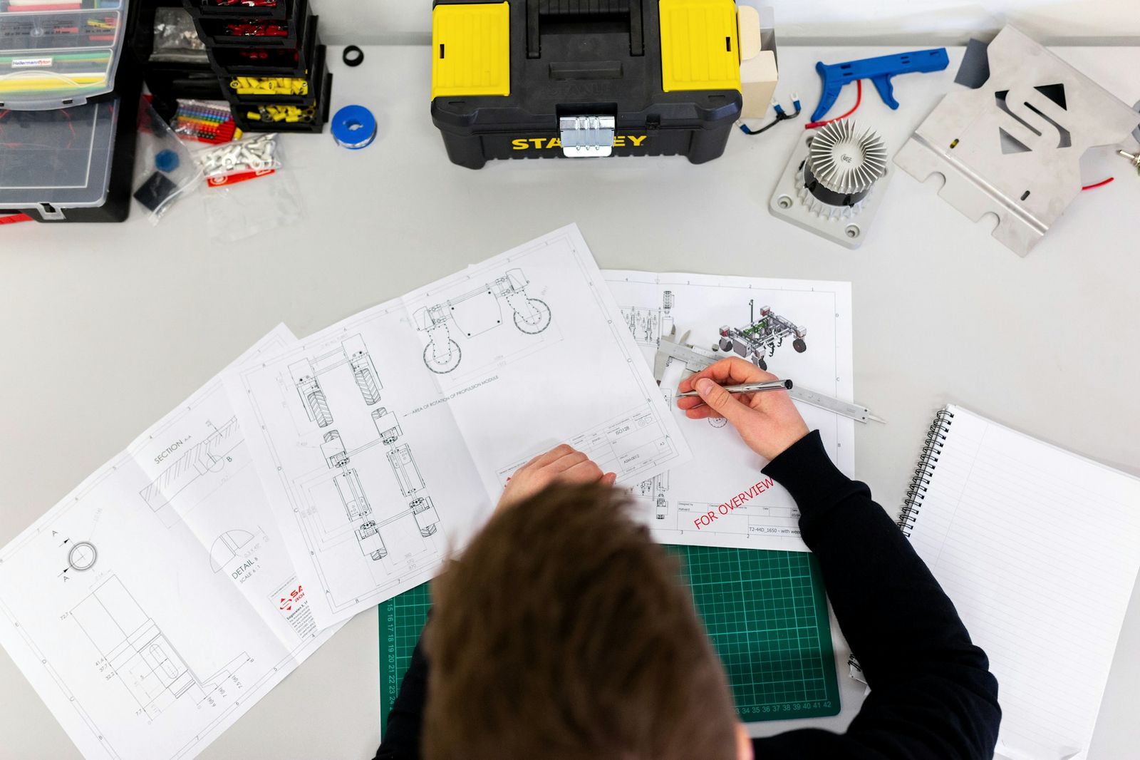 An engineer measuring a component against technical drawings at a workbench